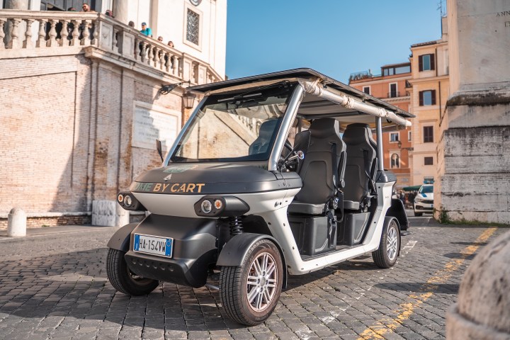 Electric golf cart parked on cobblestone street near historic buildings.