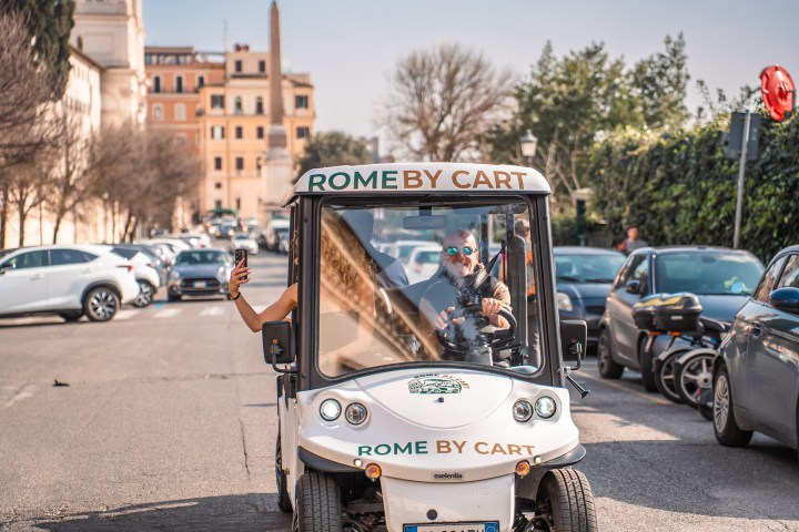 Small cart in a busy Rome street with a person taking a selfie, labeled 'Rome By Cart'.
