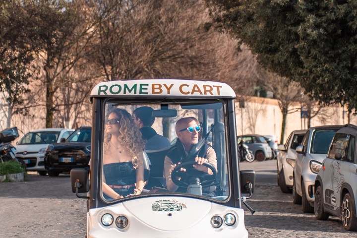 A small white cart with 'Rome by Cart' sign driving on a cobblestone street.