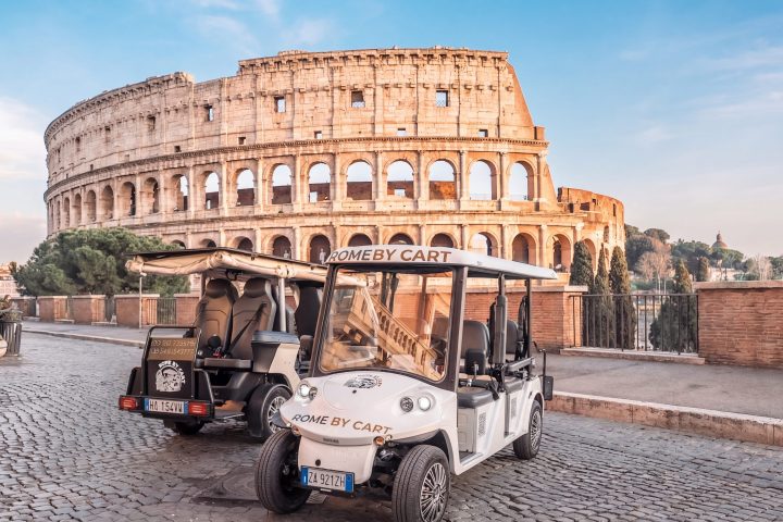 Two golf carts parked near the Colosseum in Rome under a clear sky.