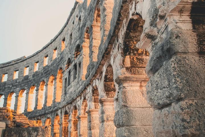 Stone archways of an ancient amphitheater lit by the setting sun.