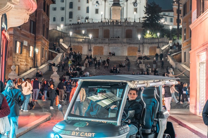 A small car with bright headlights in front of Spanish Steps at night.