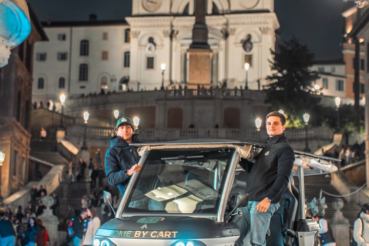 Two people stand by a golf cart near an illuminated historic building at night.