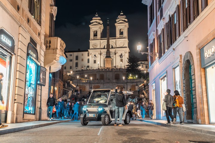 Night street scene in Rome with Spanish Steps and people walking.