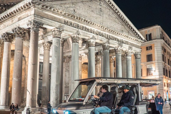 Electric cart in front of the Pantheon at night with two people seated inside.